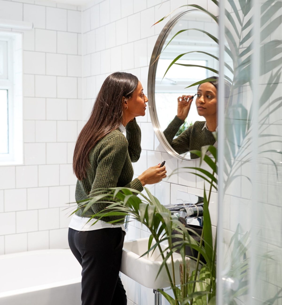 Businesswoman At Home Putting On Make Up In Mirror Before Leaving For Work